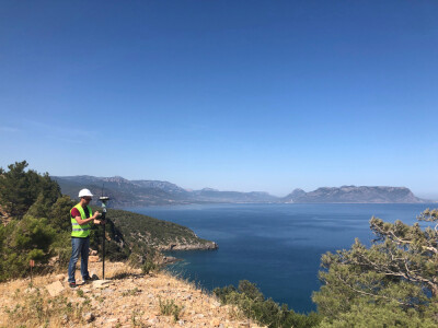 Geodetic engineer surveyor in white hard hat doing measurements with GNSS satellite receiver at the hill top above the sea