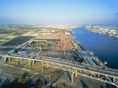 Aerial view of Corpus Christi Harbor Bridge with row of oil tanks and wind turbines farm in distance. A through arch bridge crosses the Corpus Christi Ship Channel